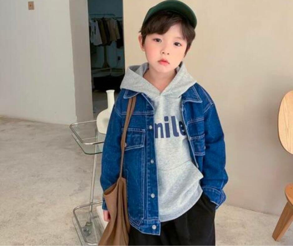 Menino de boné verde e vestindo moletom cinza com jaqueta jeans sobreposta